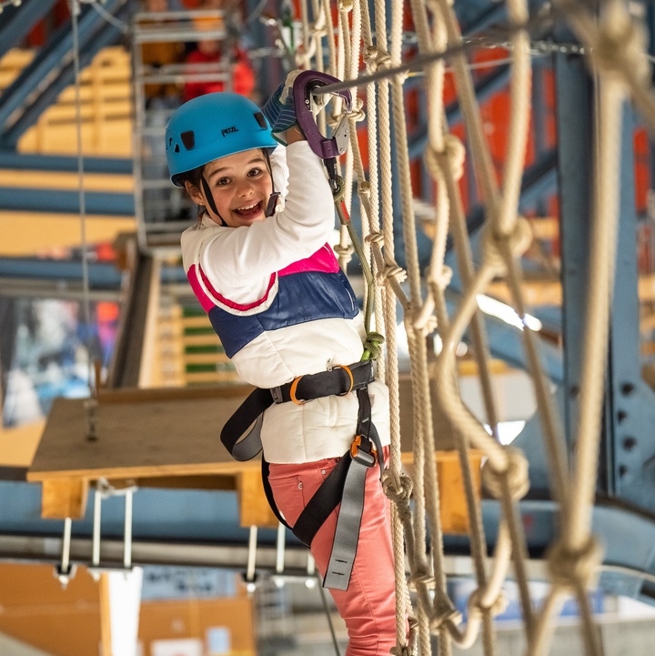 A young girl stands on a rope ladder and grabs the safety cable as she navigates a course at the Indoor Ropes Park in Grindelwald